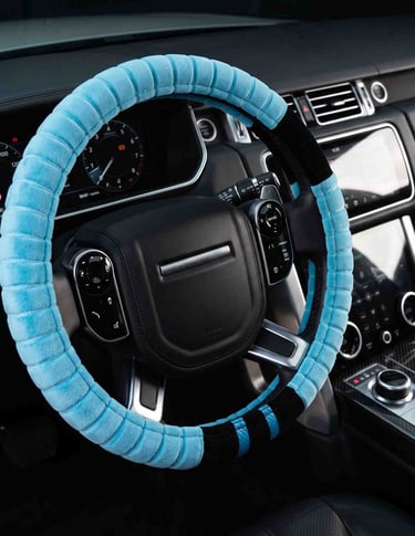 A light blue plush steering wheel cover installed on a black leather car interior for comfort and grip.