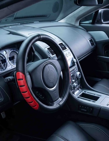 Black leather steering wheel cover with red anti-slip grips installed in a modern car interior.