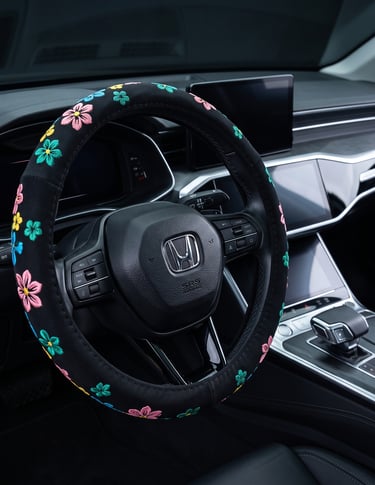 Black steering wheel with a colorful floral embroidered cover inside a modern Honda car interior.