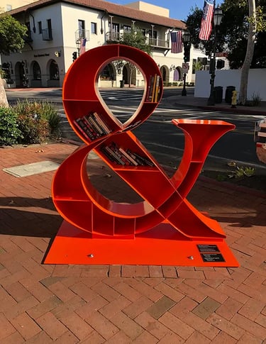 An innovative book-sharing box designed as a large red ampersand, encouraging community reading on a city street.