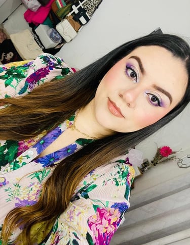 Mujer con cabello largo y oscuro que usa sombra de ojos violeta y una blusa con estampado floral 