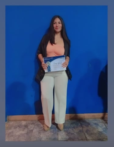 Professional woman holding a certificate of achievement in front of a blue wall background.