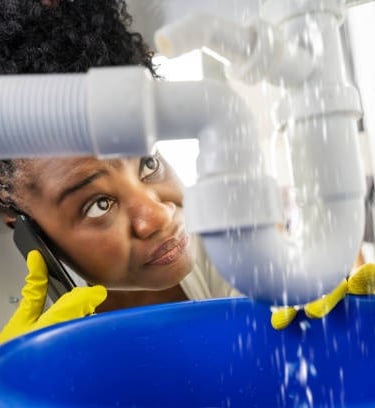 woman on the phone staring at her leaking pipe