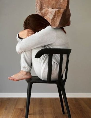 Una mujer sentada en una silla con una pesada roca sobre la espalda, que simboliza el estrés