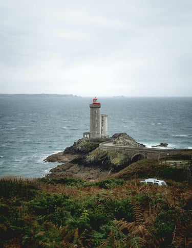 a lighthouse on a rocky island with a car parked on the side of the road