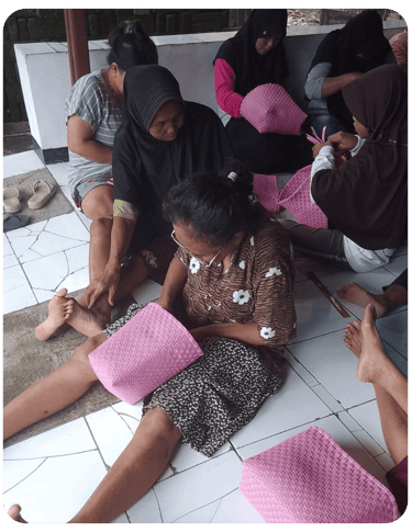 Artisan weaving a pink jali jali plastic woven bag by hand at Craftvitas Indonesia.