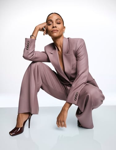 Zoe Saldana wearing a dusty rose tailored power suit and maroon stiletto heels for a fashion editorial.