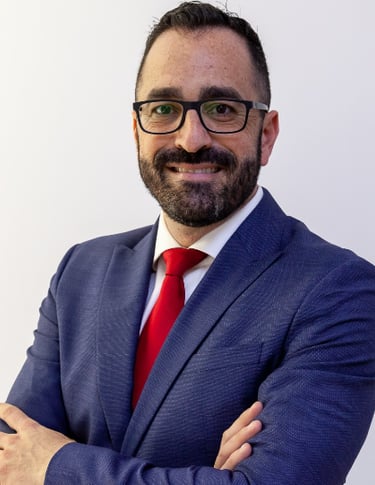 Professional headshot of a smiling businessman in a blue suit and red tie wearing glasses.