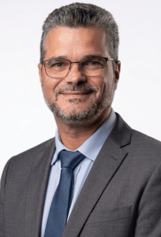 Professional headshot of a smiling businessman in a grey suit and blue tie with glasses.