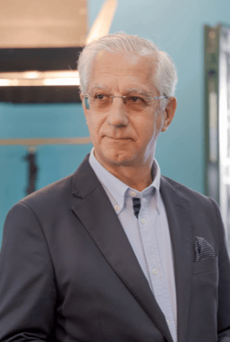 Professional senior man wearing a navy blazer and light blue shirt in a studio setting.