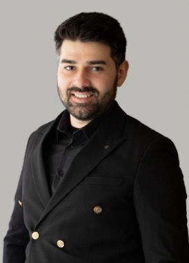 Professional headshot of a smiling man with a beard wearing a black double-breasted suit blazer.