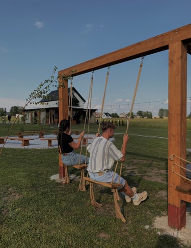 Dwie osoby na drewnianej huśtawce, a w tle domek