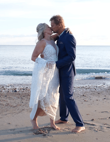 A bride and groom dance on a sandy beach 