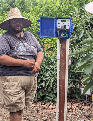 Mira Costa student explaining his water sensor project, standing next to a blue box on a wooden post