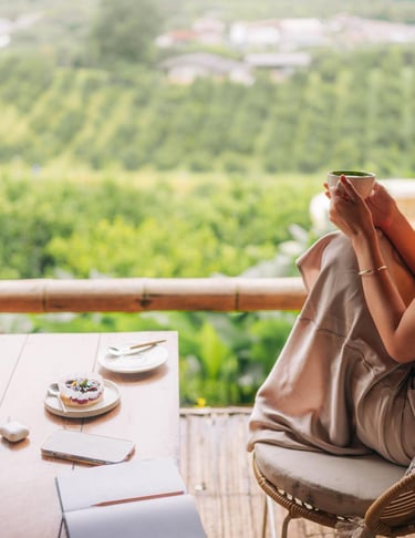 Smiling woman drinking matcha tea on a balcony overlooking a lush green valley at a mountain resort.