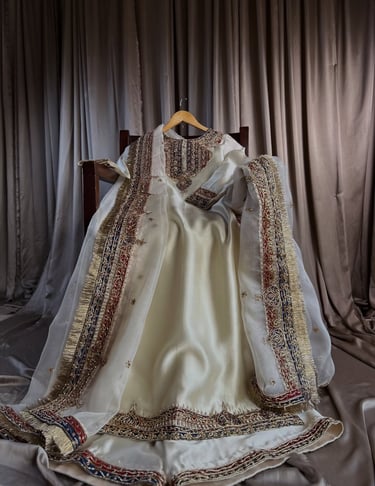 Elegant cream bridal lehenga with intricate gold embroidery and a matching dupatta on a wooden chair.