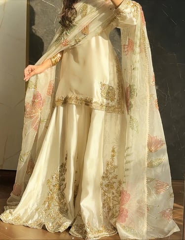 Elegant cream-colored sharara suit with gold embroidery and a floral net dupatta.