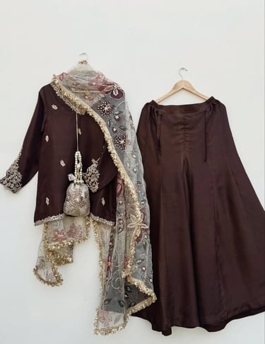 Brown Indian lehenga choli with embroidered dupatta and matching potli bag hanging on a white wall.