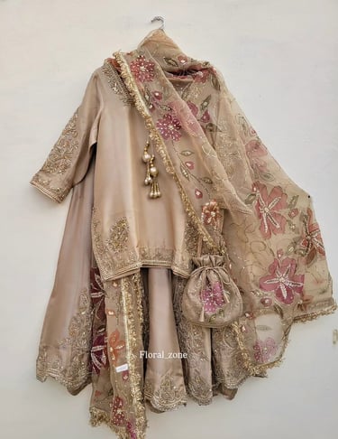 Elegant beige bridal lehenga with pink floral embroidery and a matching potli bag.