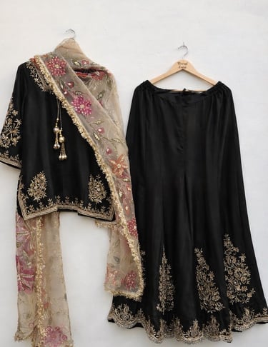 Elegant black lehenga choli with gold embroidery and a floral net dupatta on a white background.