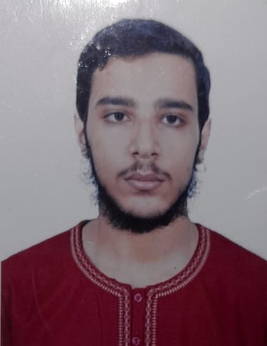 Portrait of a young man with a beard wearing a red embroidered tunic in a headshot photo.