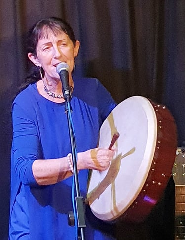 paula ryan in a blue dress is holding a drum and a microphone