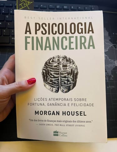 Hand holding A Psicologia Financeira book by Morgan Housel with brain shaped from money on the cover.