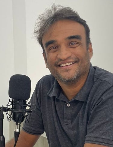 a man in a gray shirt is smiling and holding a microphone