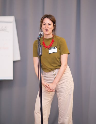 Young woman speaking behind microphone, flipchart in the back showing teachings of seminar