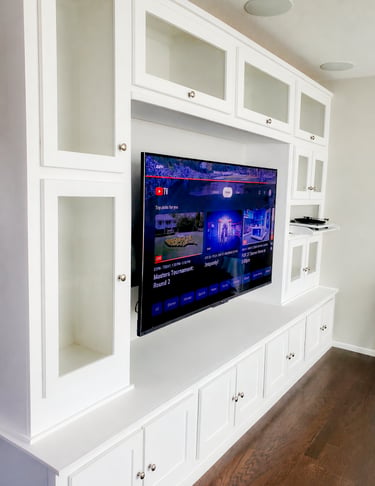 Modern white custom built-in entertainment center with glass cabinets and a wall-mounted TV.
