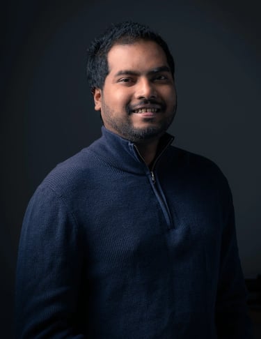 Professional headshot of Tharinda H.A smiling in a navy sweater against a dark gray background.