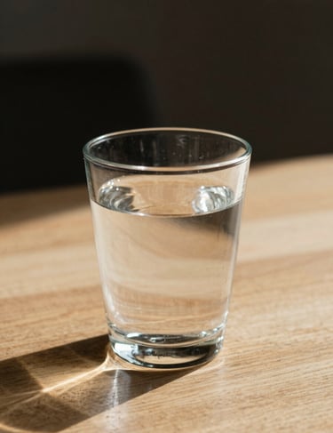Sunlight hitting a glass of water on a wooden table, artistic lifestyle shot, cinematic focus, warm #FDF8F0 light.