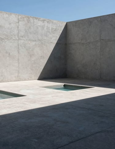 Bright, direct sunlight hitting a minimalist light grey concrete courtyard in Brazil. Sharp, dark charcoal shadows create artistic patterns on the floor. A single small pool of water reflects the baby blue sky.