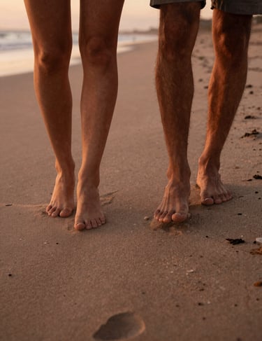 A cinematic close-up of a couple's feet walking on a sandy North American / US shoreline. Warm terracotta sunset tones, soft sand underfoot.
