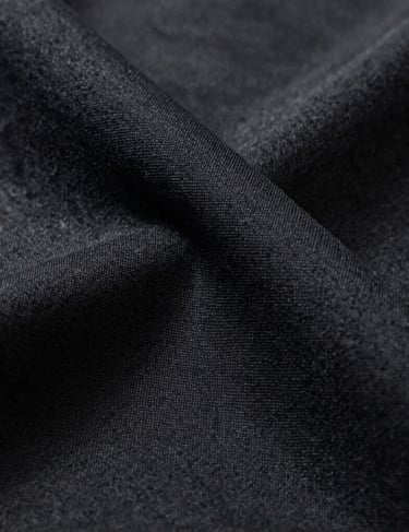 A close-up shot of a luxury fabric texture in deep charcoal and black, dramatic side lighting highlighting the quality and detail, North American studio style.