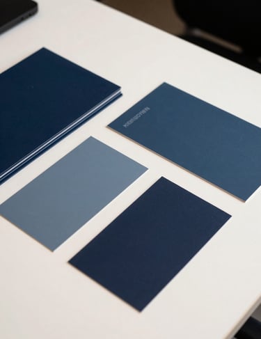 A flat lay of brand guidelines and color swatches in dark slate blue and muted steel blue on a crisp off-white desk in a South American / Brazilian creative agency.