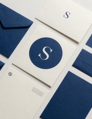 A collection of branded stationery for a luxury studio, showing logo variations in indigo blue on ivory paper, arranged in a minimalist flat lay.