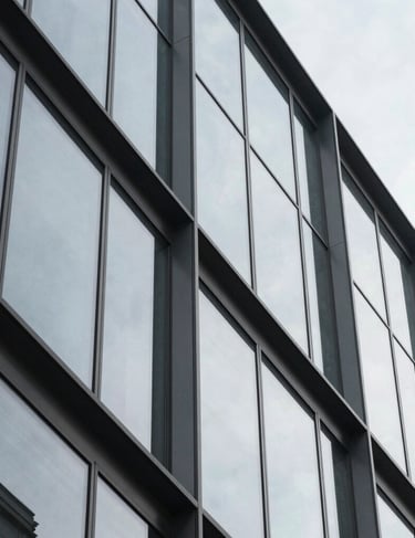 Abstract architectural detail of a modern glass building featuring sharp geometric shapes and reflections in light gray tones. International / Professional.