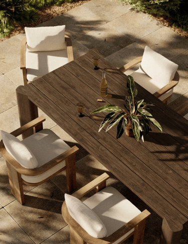 Outdoor wooden table with cushioned chairs, plant centerpiece and natural stone flooring, creating a