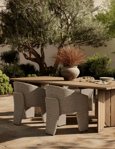Small outdoor table surrounded by woven chairs, olive tree and warm garden plants for relaxed slow l