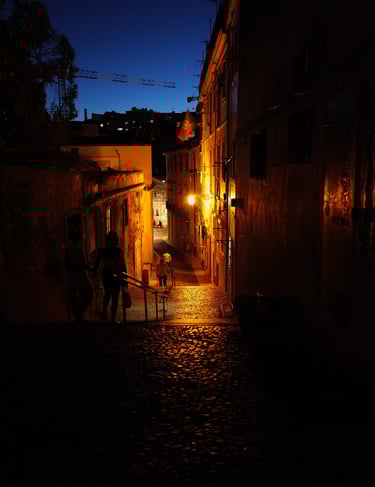 Night cobblestone alley lit of Lisbon by warm streetlights with walking silhouettes, By ACAT Photos