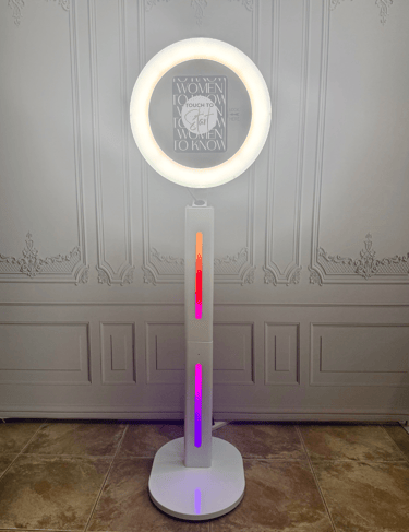 White ring light photo booth stand with colorful LED accent lights and a touch screen for events.