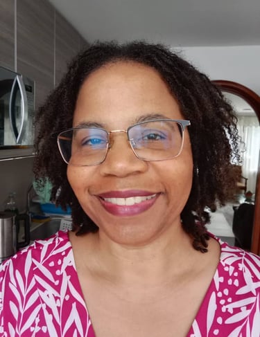 Smiling woman with dark microlocs and glasses wearing a pink and white floral pattern shirt.