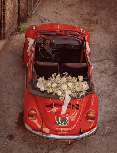 Auto d’epoca rossa decorata con fiori bianchi e nastri, pronta per il matrimonio