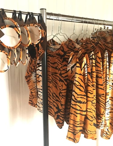 Tiger print costume sets including shirts, leggings, and ears hanging on a garment rack.