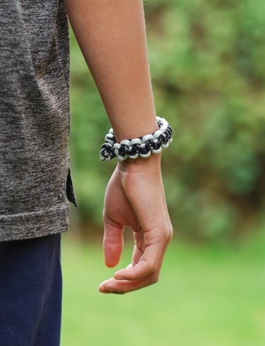 a paracord bracelet on a person's wrist with a green nature background