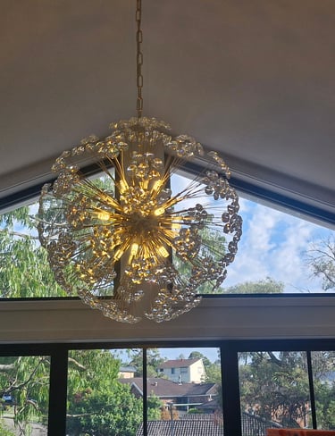 Modern gold starburst chandelier hanging from a vaulted ceiling in front of large windows.