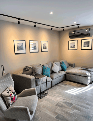 Sala moderna con sofá gris en L, cuadros en blanco y negro y lámparas tipo riel | KARÄNA