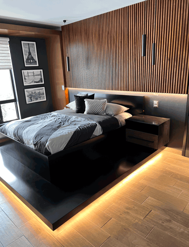 Recámara de lujo con iluminación LED en plataforma, muro de madera y cama en negro mate | KARÄNA