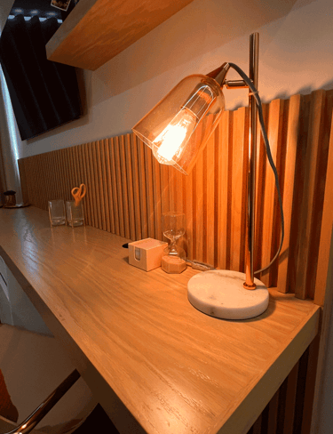 Escritorio de madera con iluminación cálida, lámpara moderna y detalles decorativos | KARÄNA